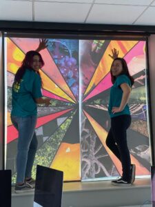 two women posing with large art piece